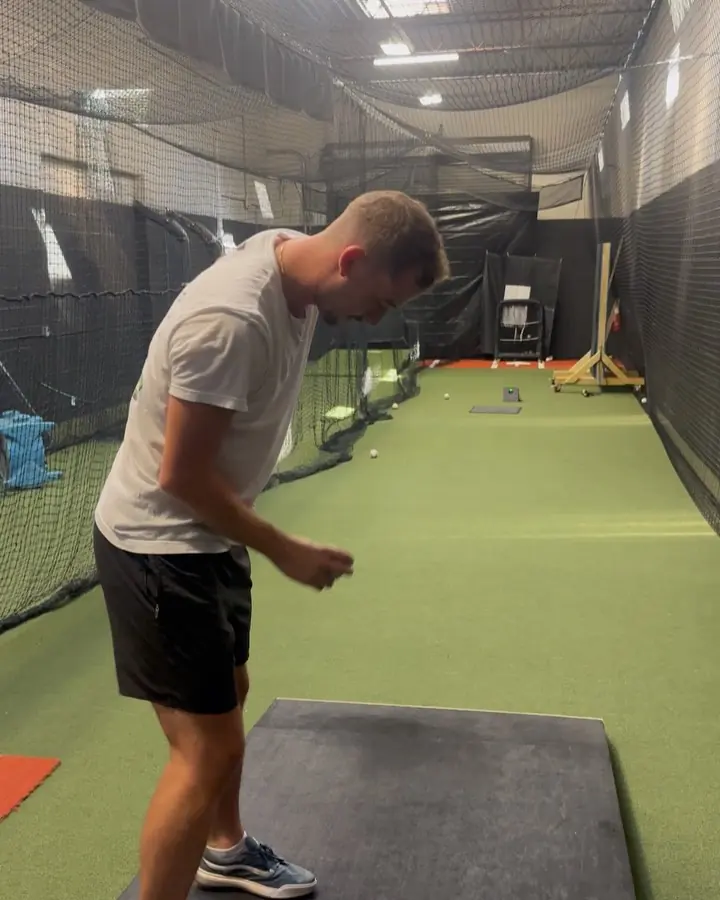 Coach running an arm care movement on the turf lane inside the facility