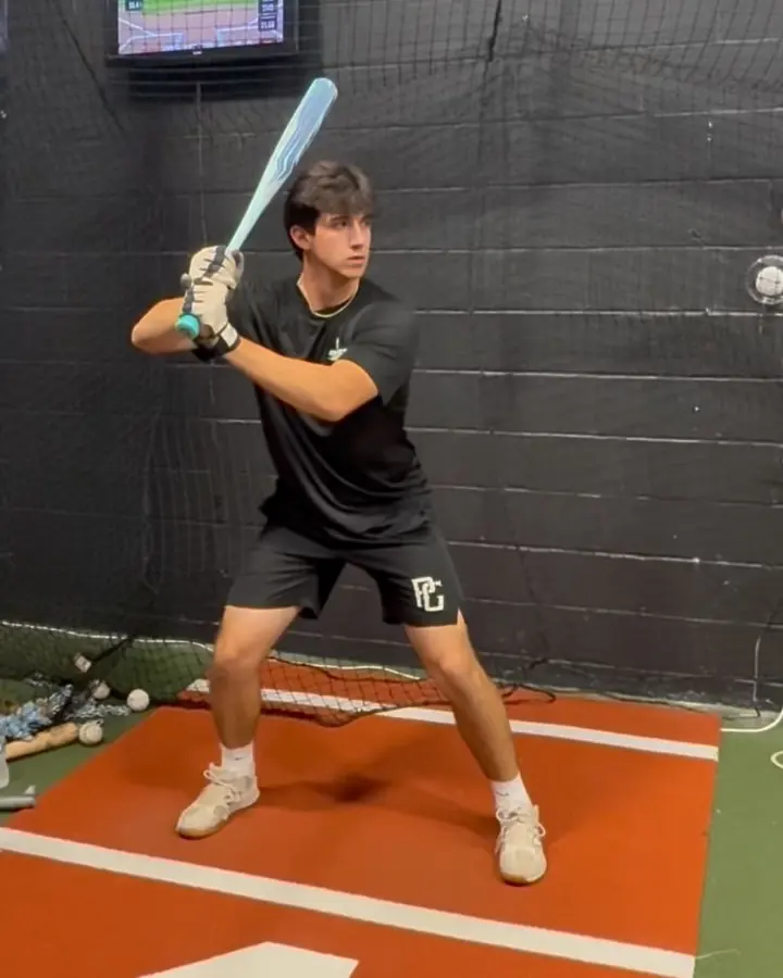 High school hitter loaded in his stance in the tracked cage, blue bat on his shoulder