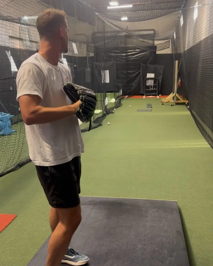 Coach in a white shirt finishing a throw on the green turf lane at the Lindenhurst facility